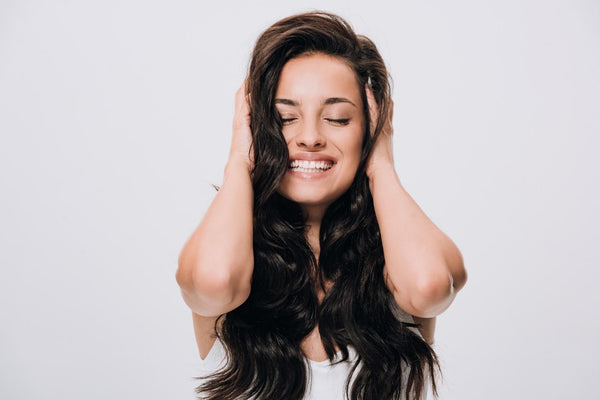 A brunette girl is smiling and touching her hair 