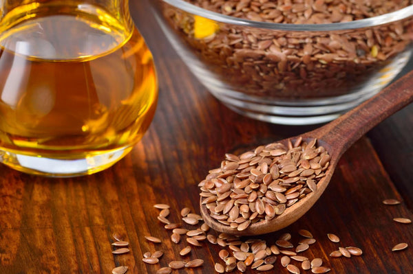 A spoon full of flax seeds next to a bowl of oil