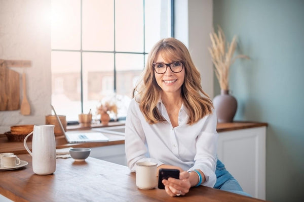 A woman sits at the kitchen table, smiling and surfing the Canaherb™ website to buy herbal supplements